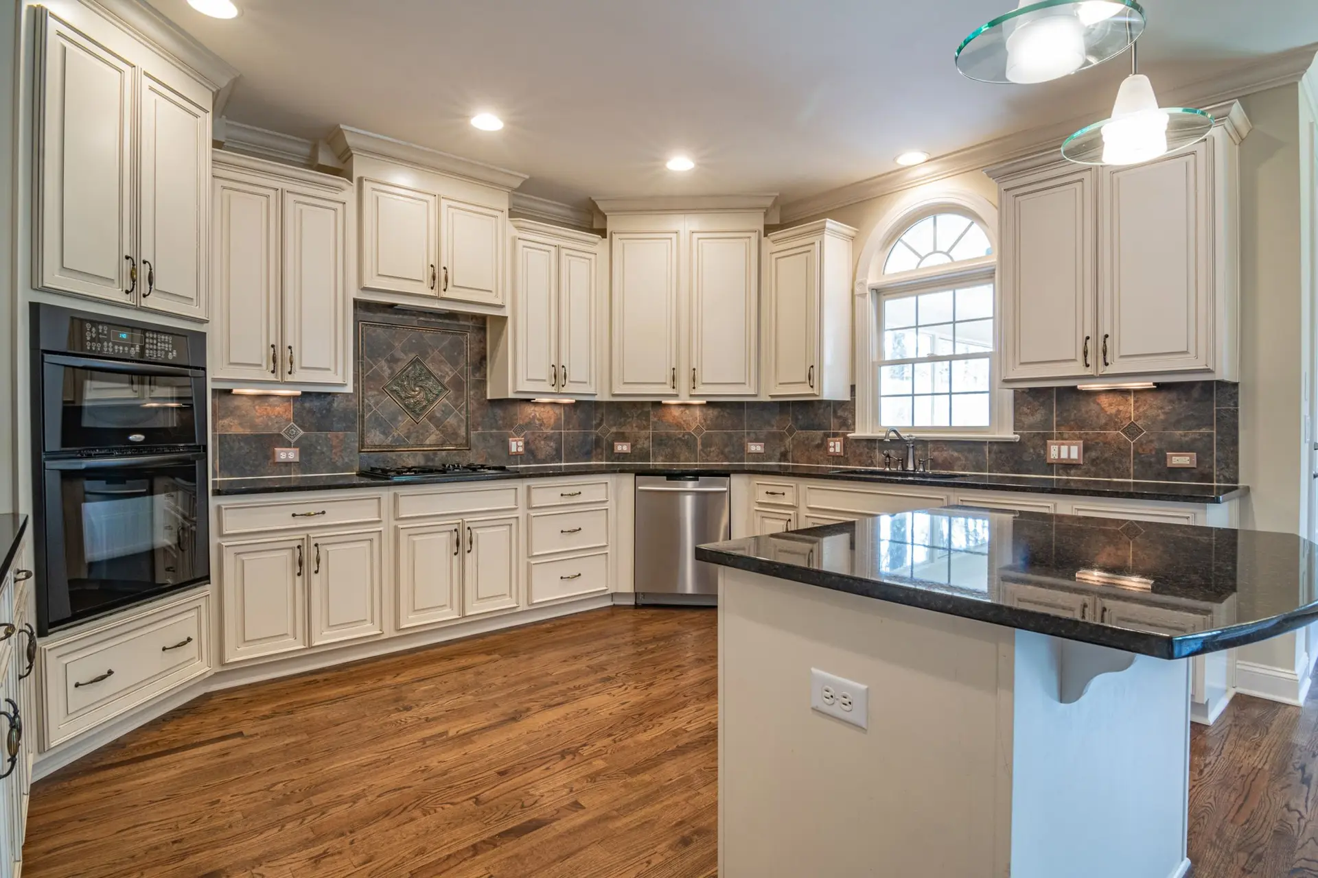Kitchen with white cabinets, a dark island top and wood floors