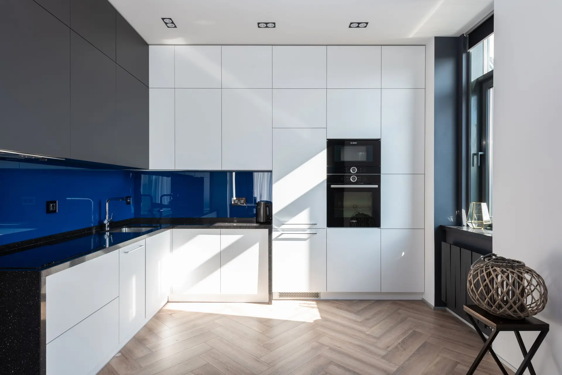 White kitchen with a cobalt glass backsplash and a herringbone floor
