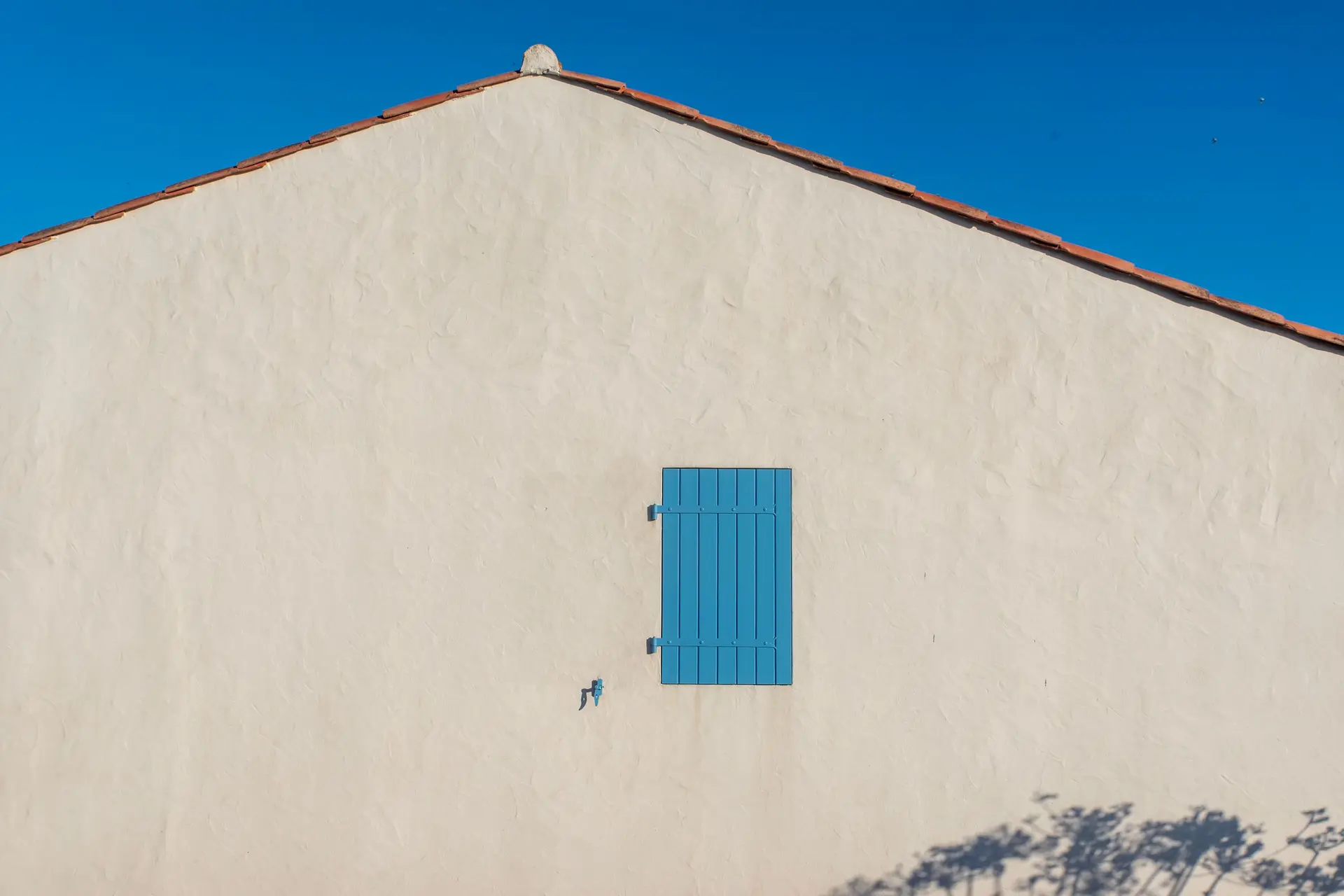 Smooth beige stucco wall with a single blue shutter